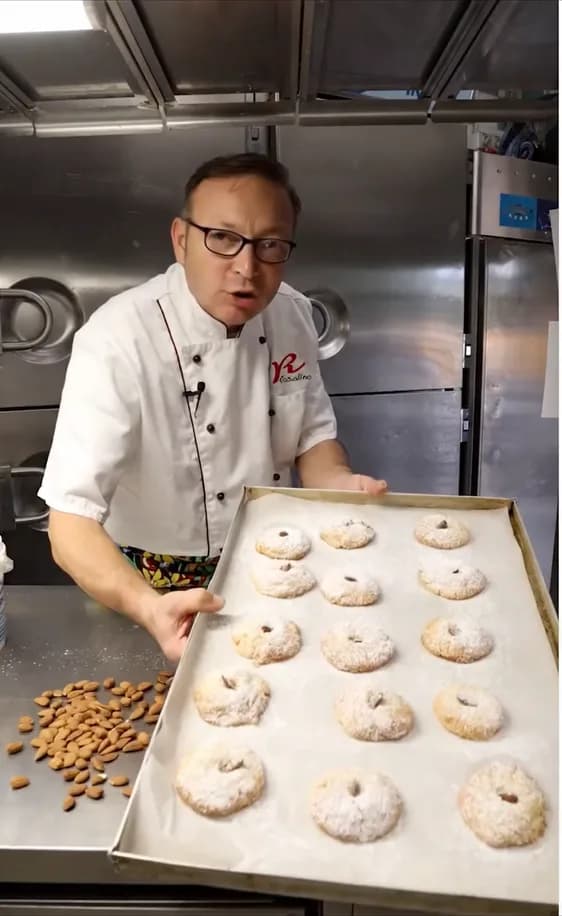 Il pasticcere mostra una teglia di biscotti alle mandorle appena sfornati